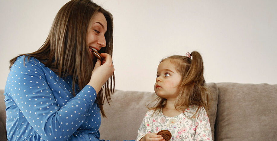 Mother teach her little daughter how to eat chocolate